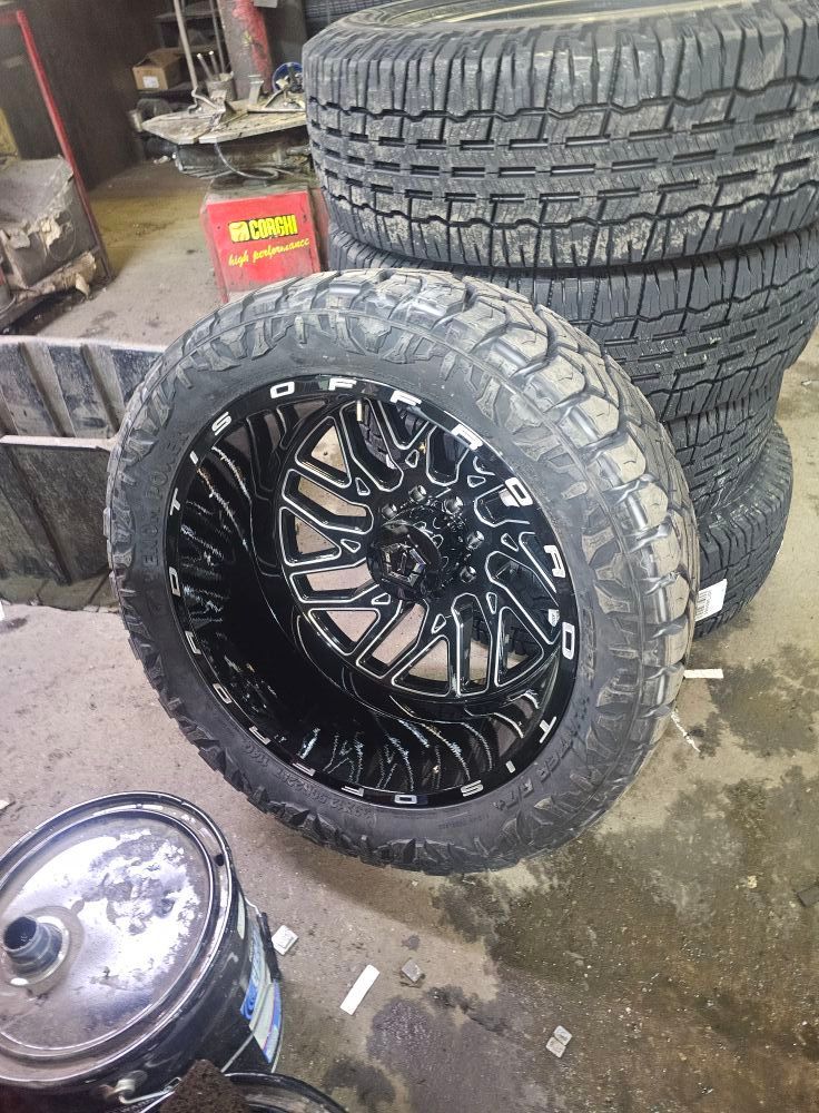 Black rim and tire, stacked tires in the background, mechanic shop setting.
