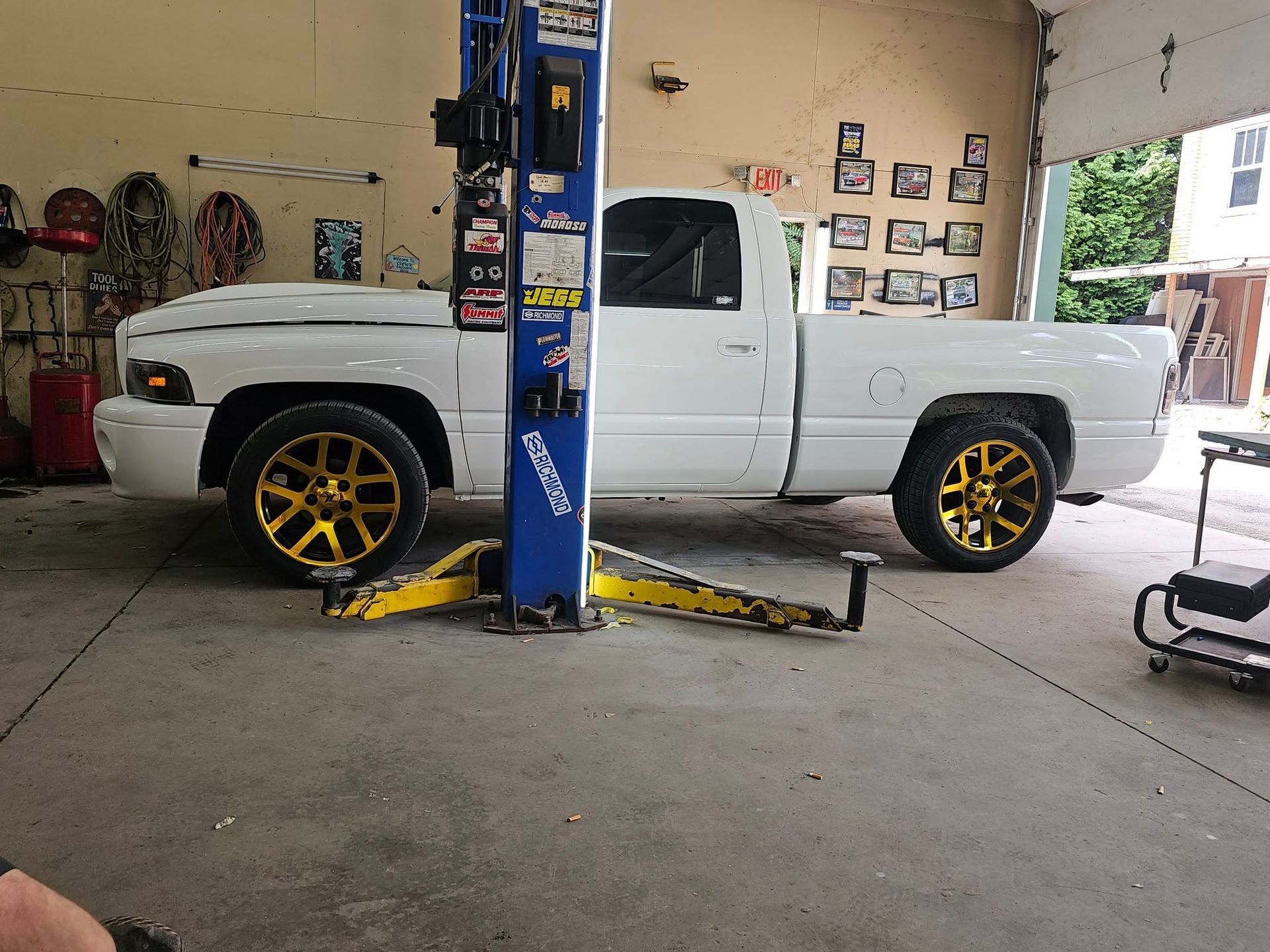 White pickup truck with gold wheels raised on a car lift in a garage.