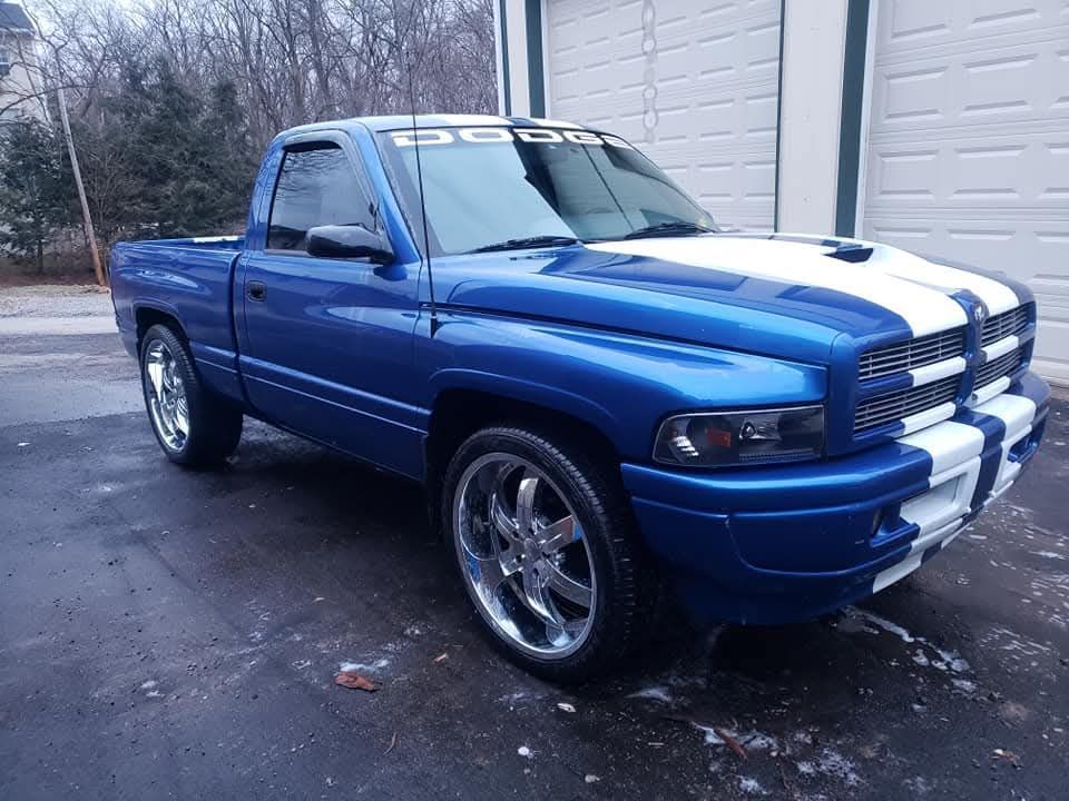 Blue Dodge Ram pickup truck with white racing stripes. Parked in front of a garage.