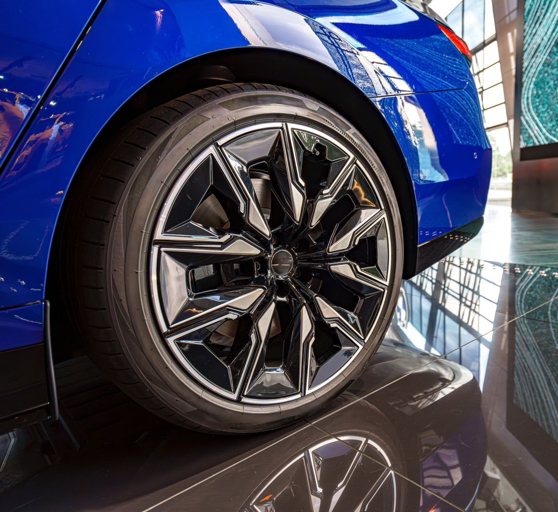 Blue car wheel with black and silver rim, reflected on shiny floor.
