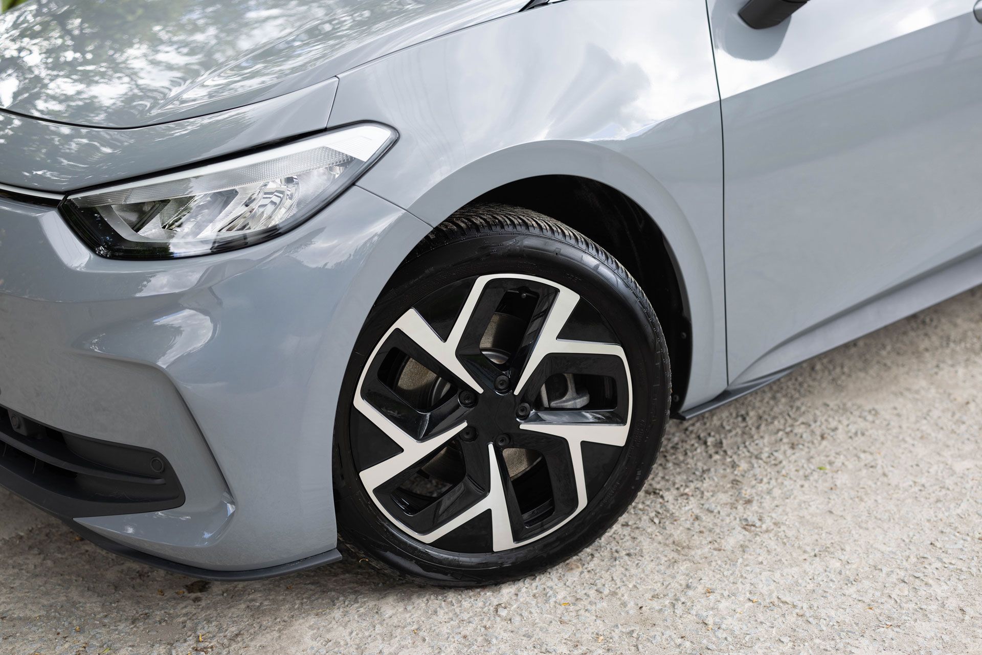 Gray car front, detail view of the wheel. Black and white patterned rim, gray body.