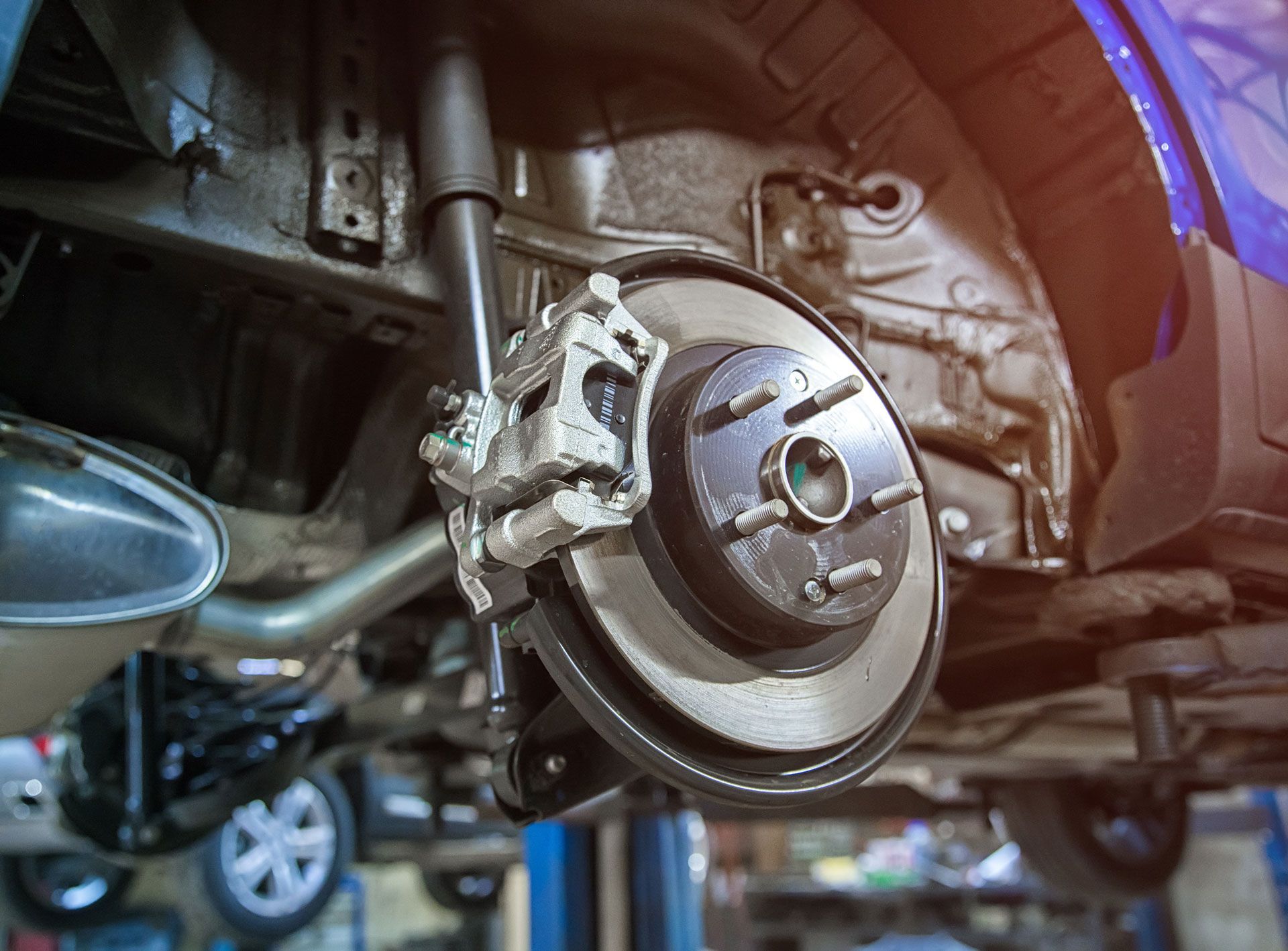 Car's rear wheel brake assembly, showing rotor, caliper, and shock absorber, viewed from below.