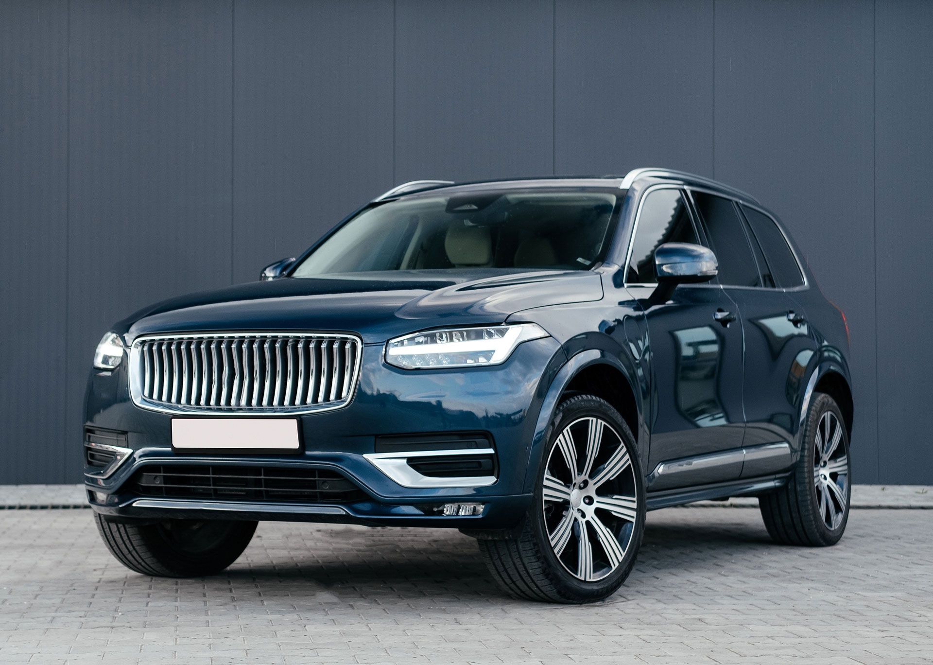 Dark blue Volvo SUV parked in front of a gray wall.