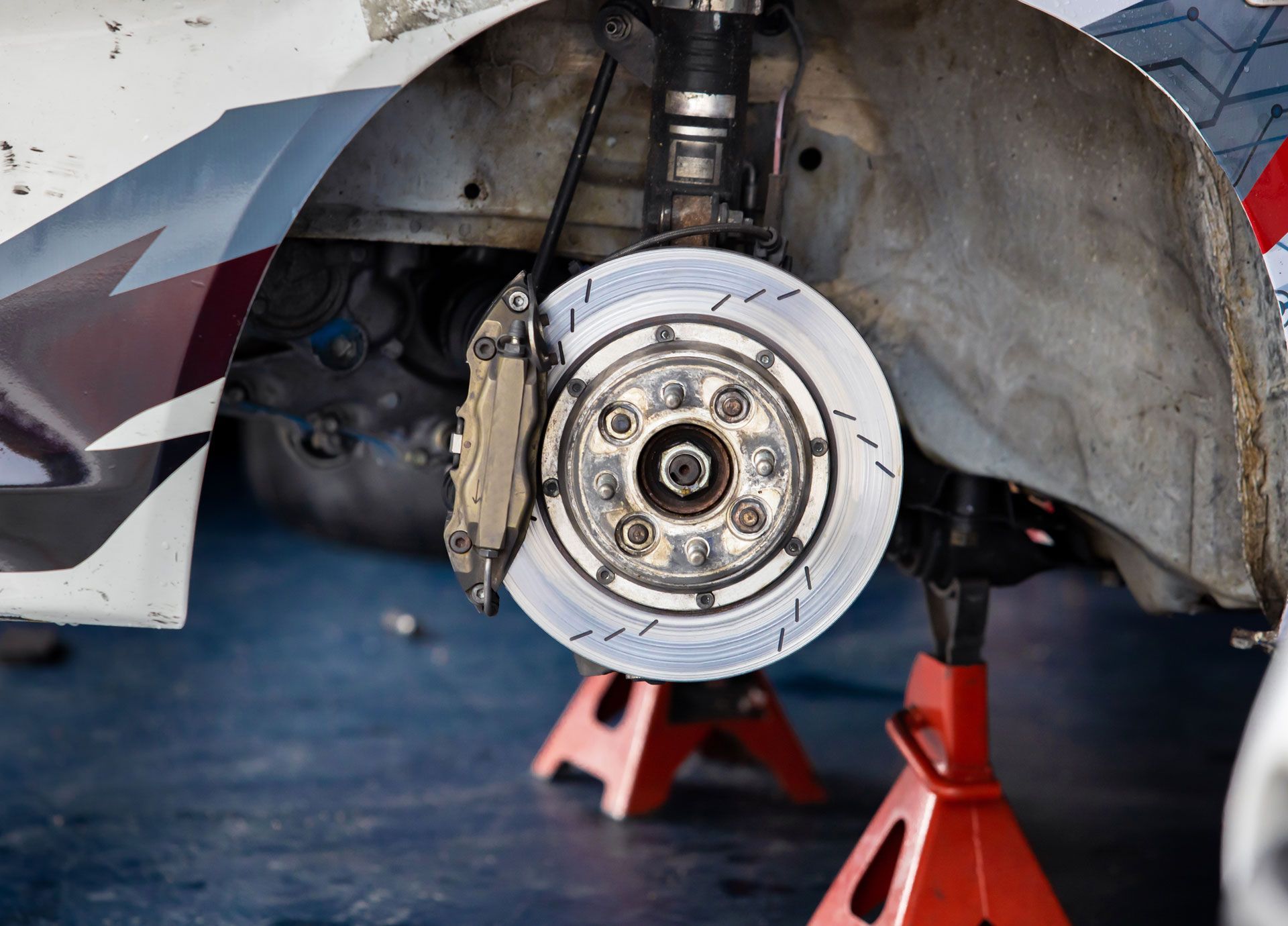 Car's front suspension with brake disc and caliper, raised on jack stands for maintenance in a garage.