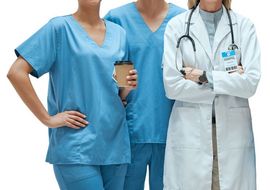 Tres trabajadores sanitarios con uniformes azules y bata blanca, uno de ellos sosteniendo un café y el otro con los brazos cruzados, todos sonriendo.