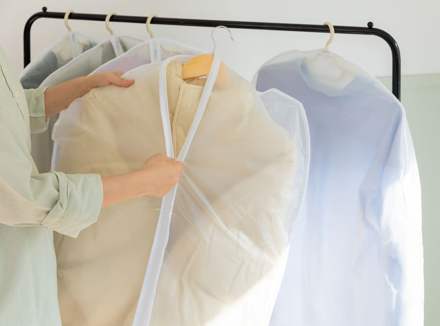 A person hanging garments protected in semi-transparent white fabric covers on a clothing rack.