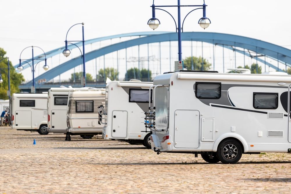 White camper trailers parked by a blue arched bridge on a cobblestone lot