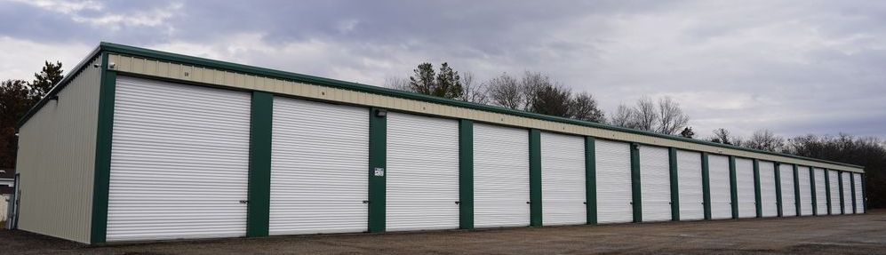 A row of storage units with green and white doors on a cloudy day.