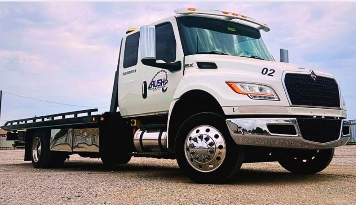 White flatbed tow truck parked on gravel, logo on door.