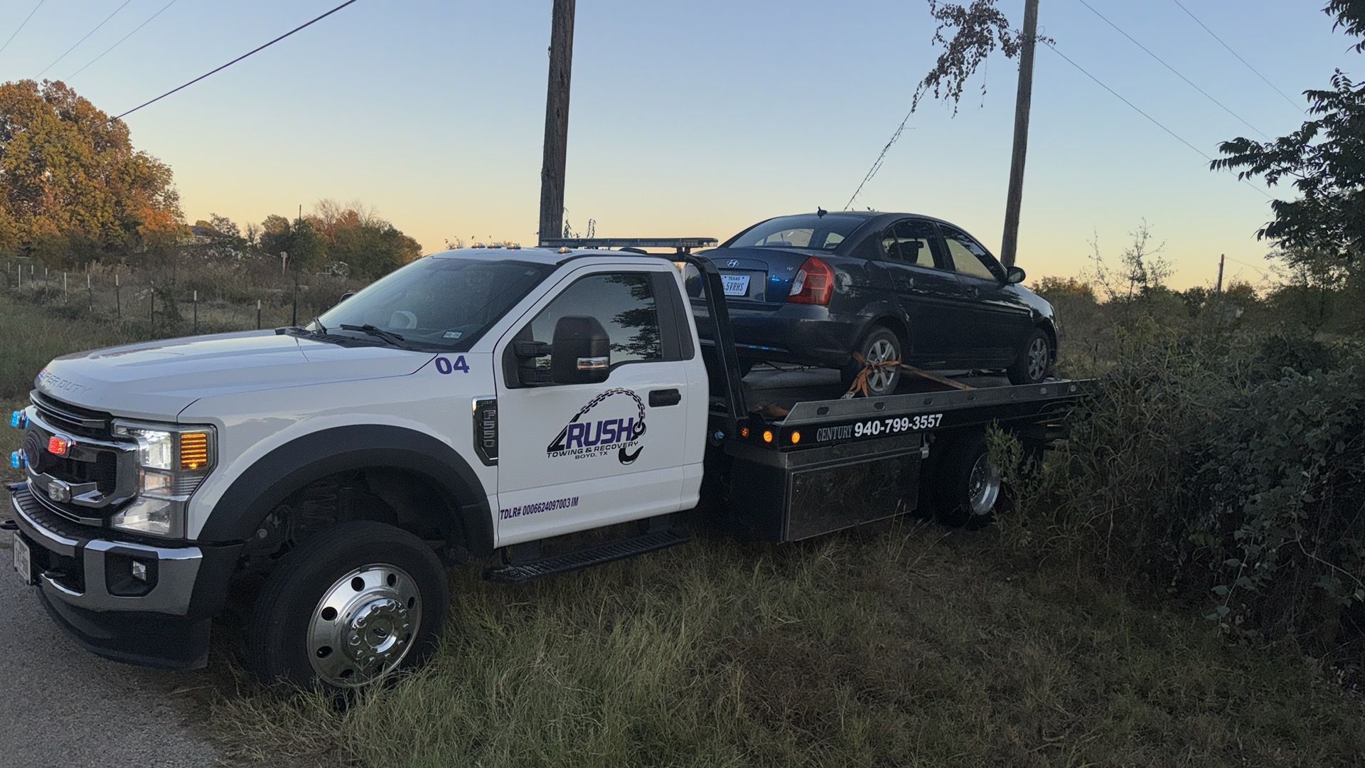 Tow truck carrying a black car, parked on the side of a road.