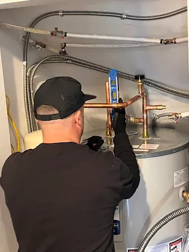 Technician adjusting copper pipes on a gray water heater in a utility room