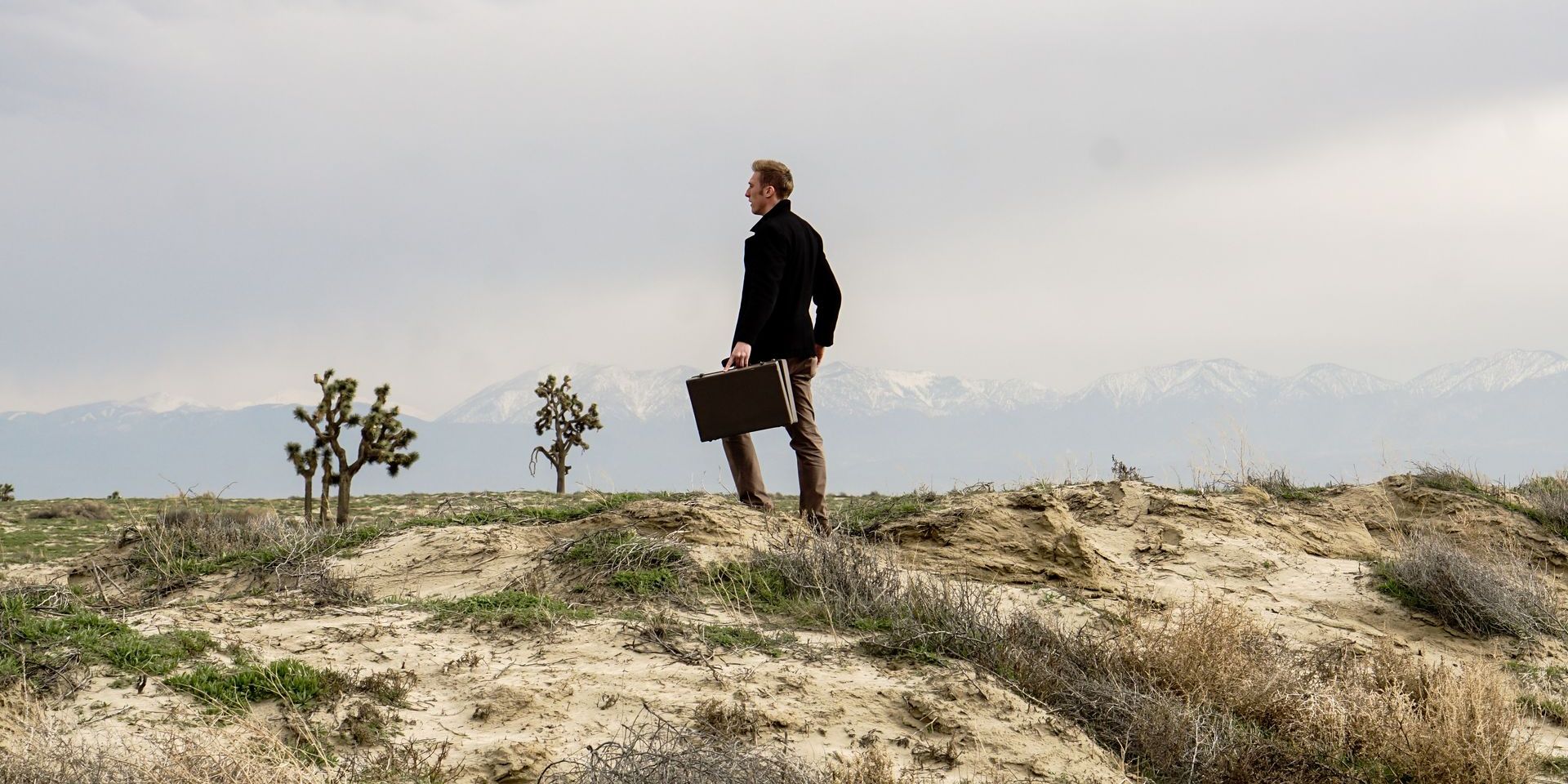 a man is standing on top of a dirt hill holding a briefcase .