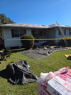 House under construction, roof partially removed. Yellow tape surrounds the damaged area. Ladder leans against the roof.