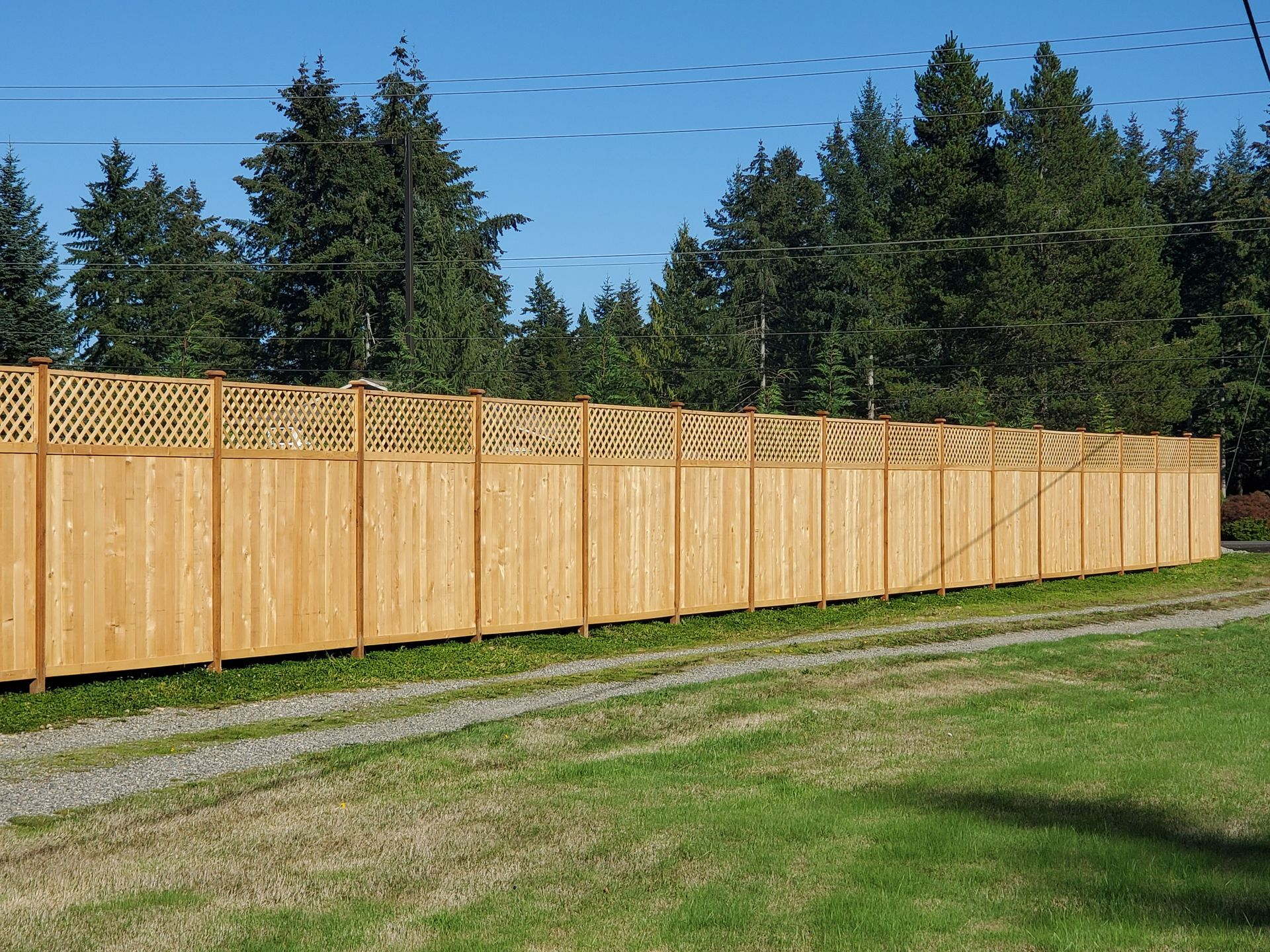 Long wooden privacy fence with lattice top along a grassy yard under a blue sky