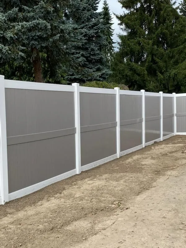 White vinyl fence along a dirt path with evergreen trees in the background