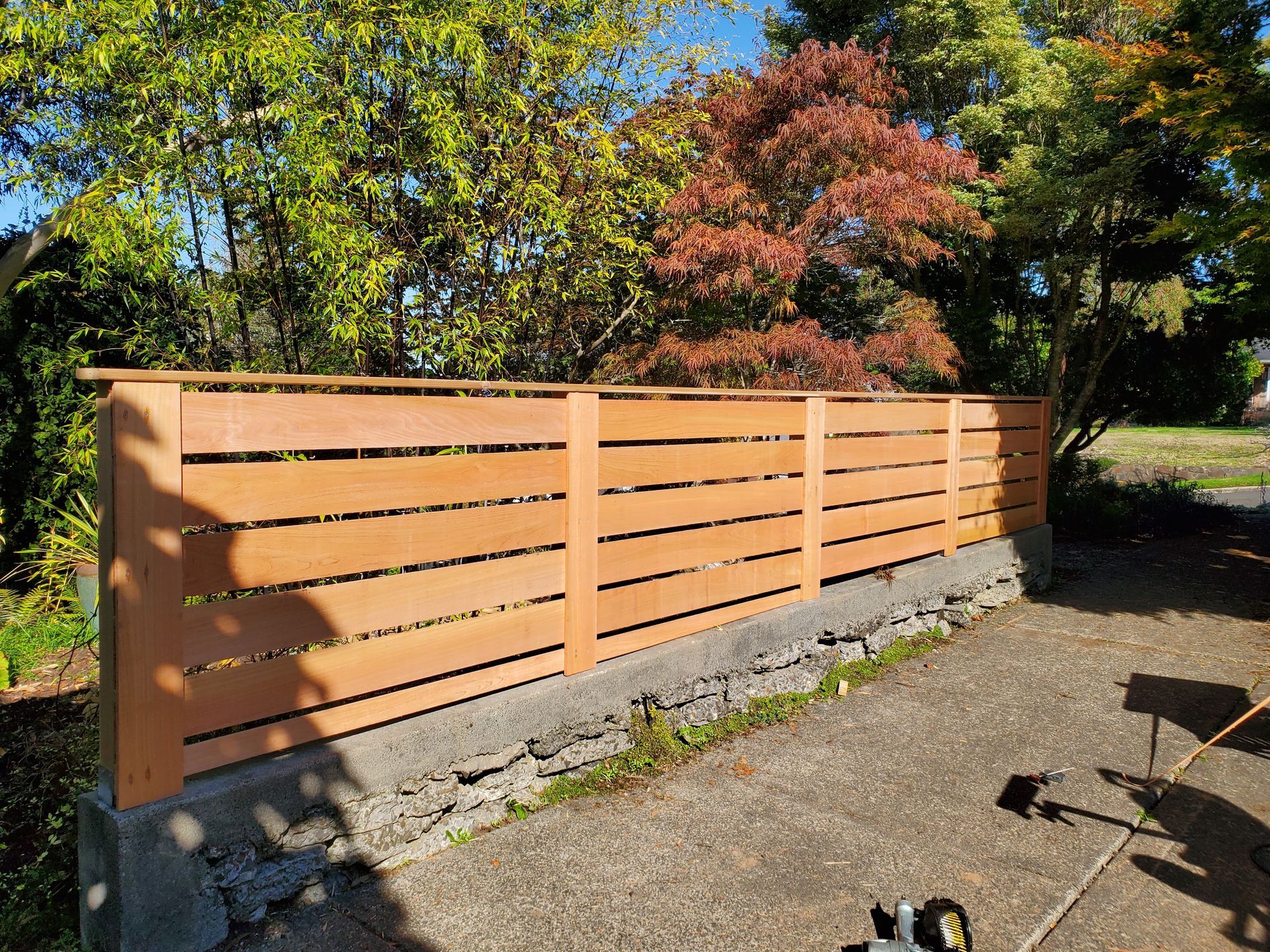 Wooden slat fence beside a gravel path, with trees and autumn foliage in the background.