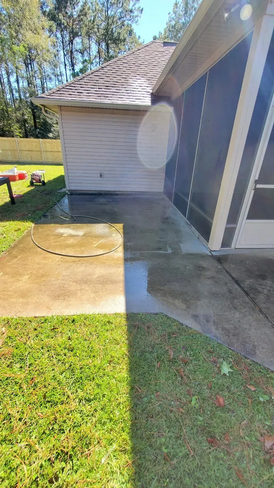 A patio with a clean, pressure-washed strip next to an uncleaned area, adjacent to a house wall and screened enclosure.