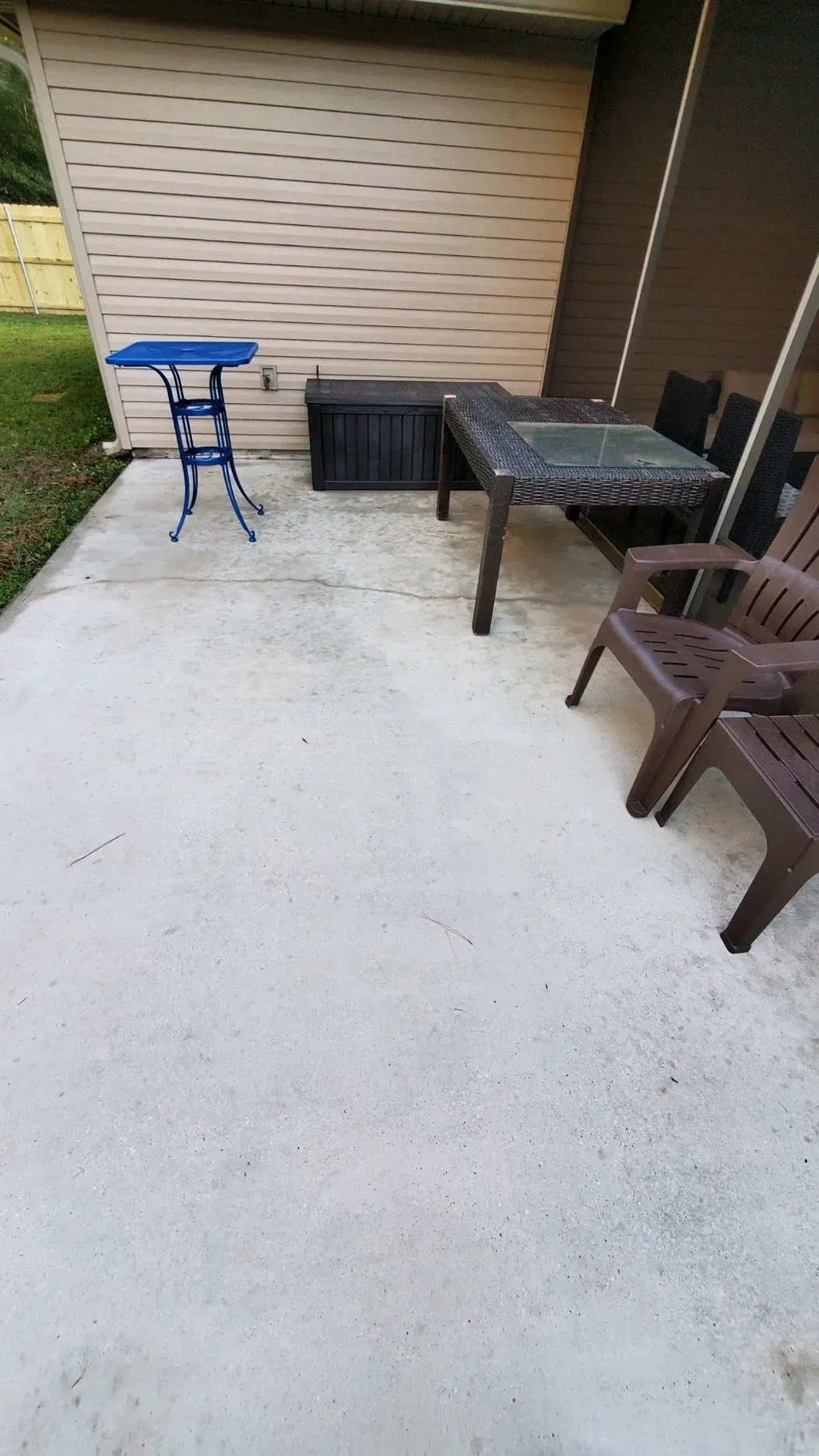 A concrete patio with a blue accent table, a black storage trunk, a table with chairs, and a neutral-colored wall.