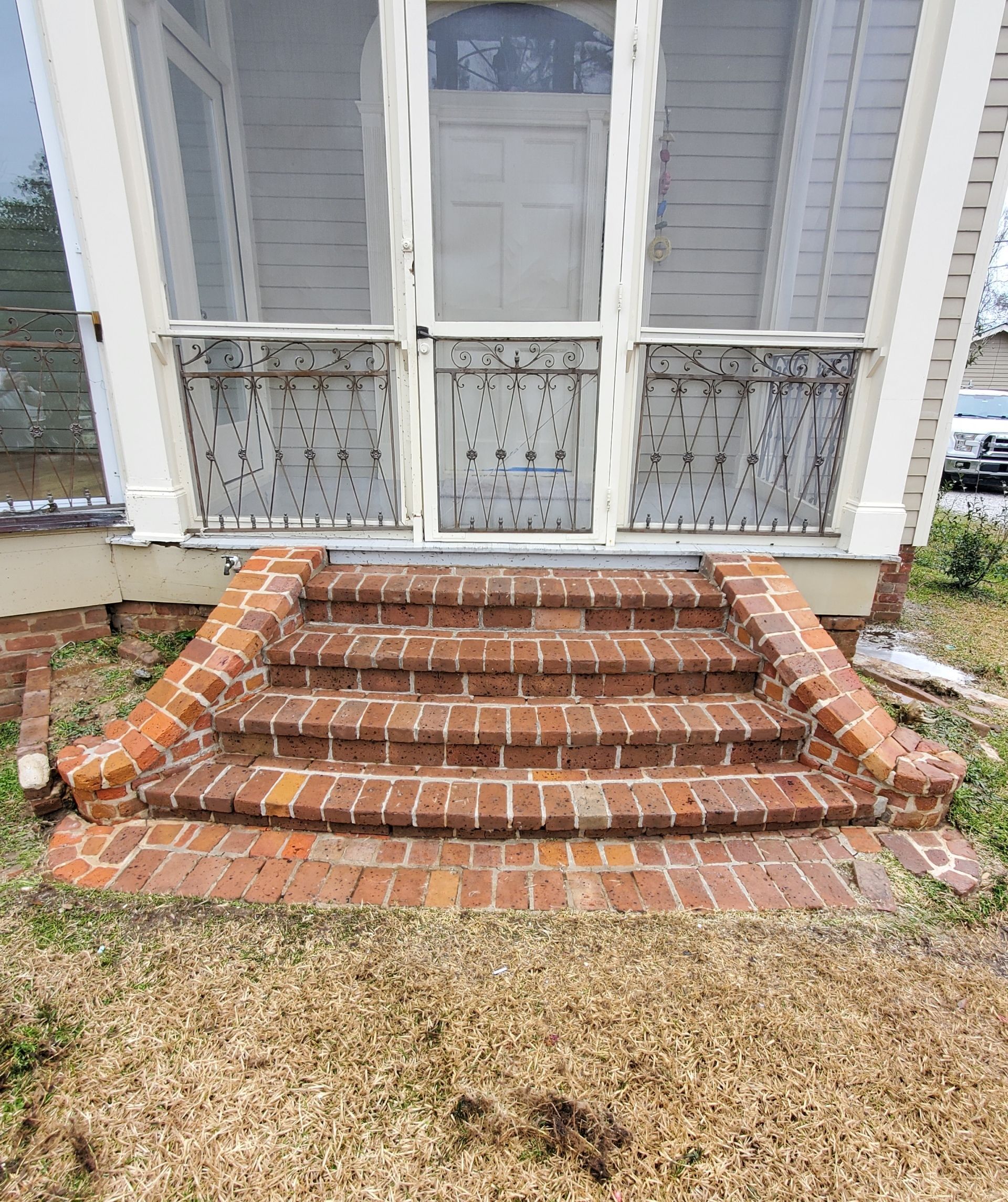 Front entrance of a house with a screen door and brick steps leading up to the porch.