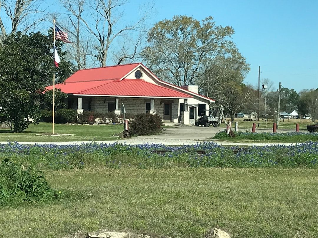 A building with a bright red metal roof and a wrap-around porch set in a grassy field with a clear blue sky.