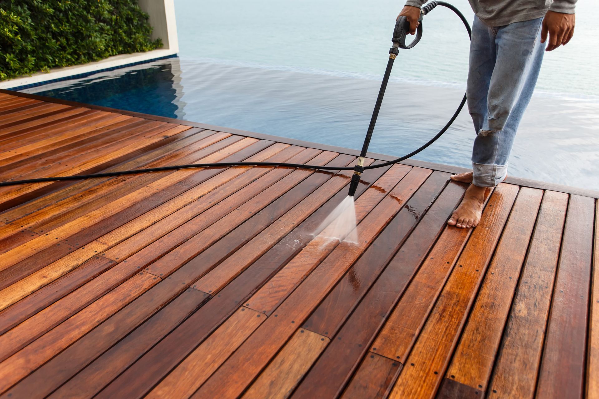 A person cleaning a wooden pool deck with a pressure washer.