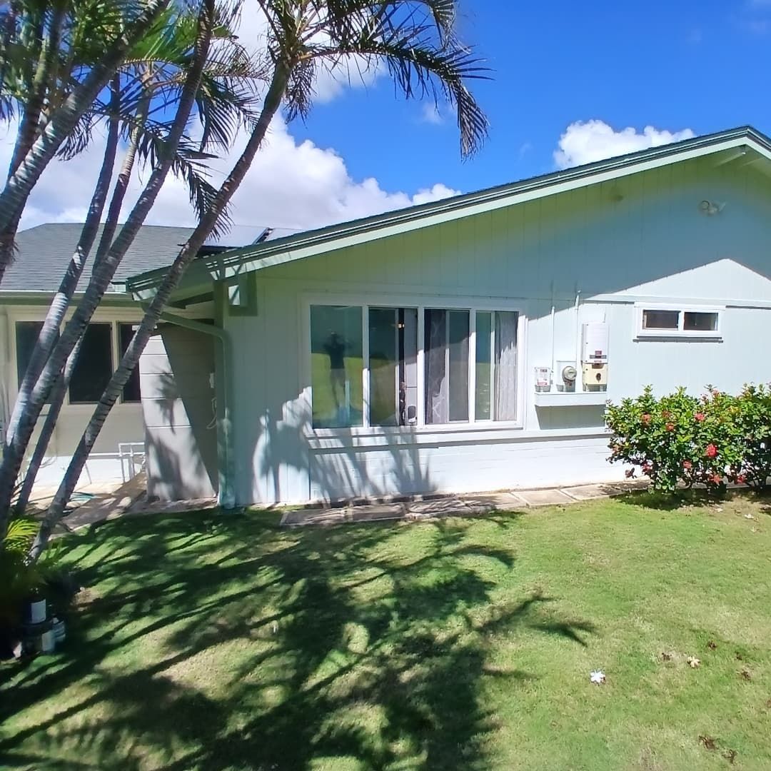 A light green house with a dark green roof trim and white-framed windows on a bright sunny day
