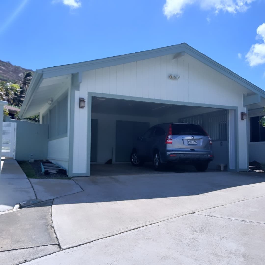 A light blue house with a large carport sheltering a silver SUV on a sunny day.