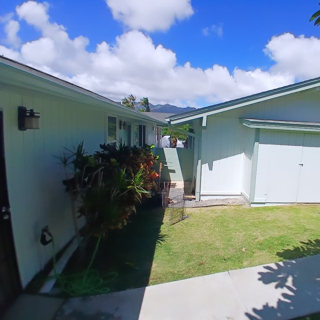 Exterior view of two light green buildings with a walkway and green grass under a blue sky with puffy white clouds.