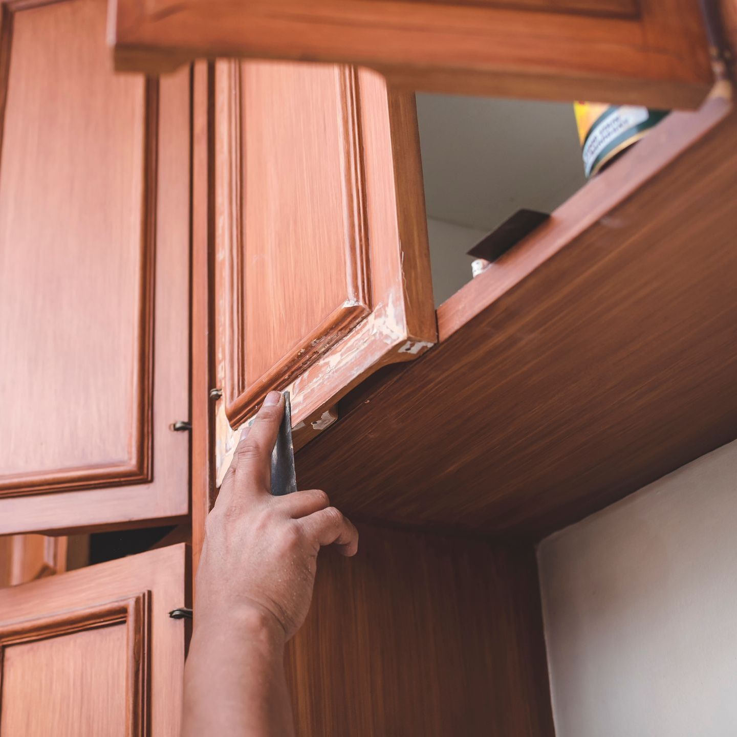 A person is fixing a kitchen cabinet with a screwdriver.
