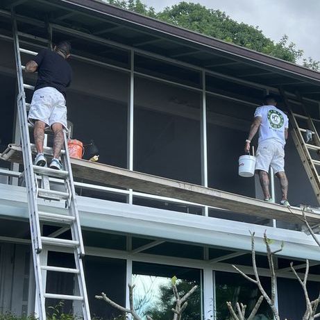 Two men painting the exterior of a building while standing on ladders and a scaffold
