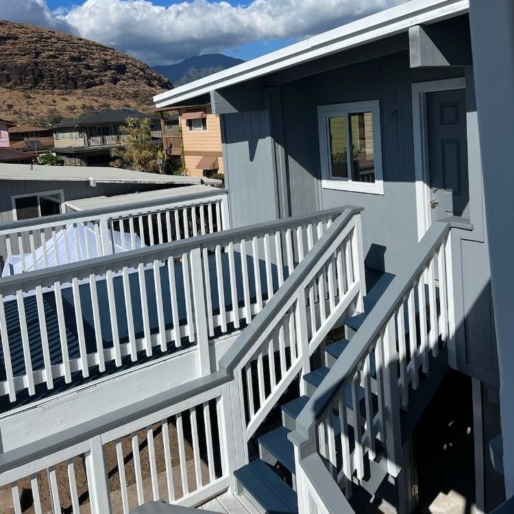 Gray building exterior with white railings, stairs, and a small window. Mountains are visible in the background.