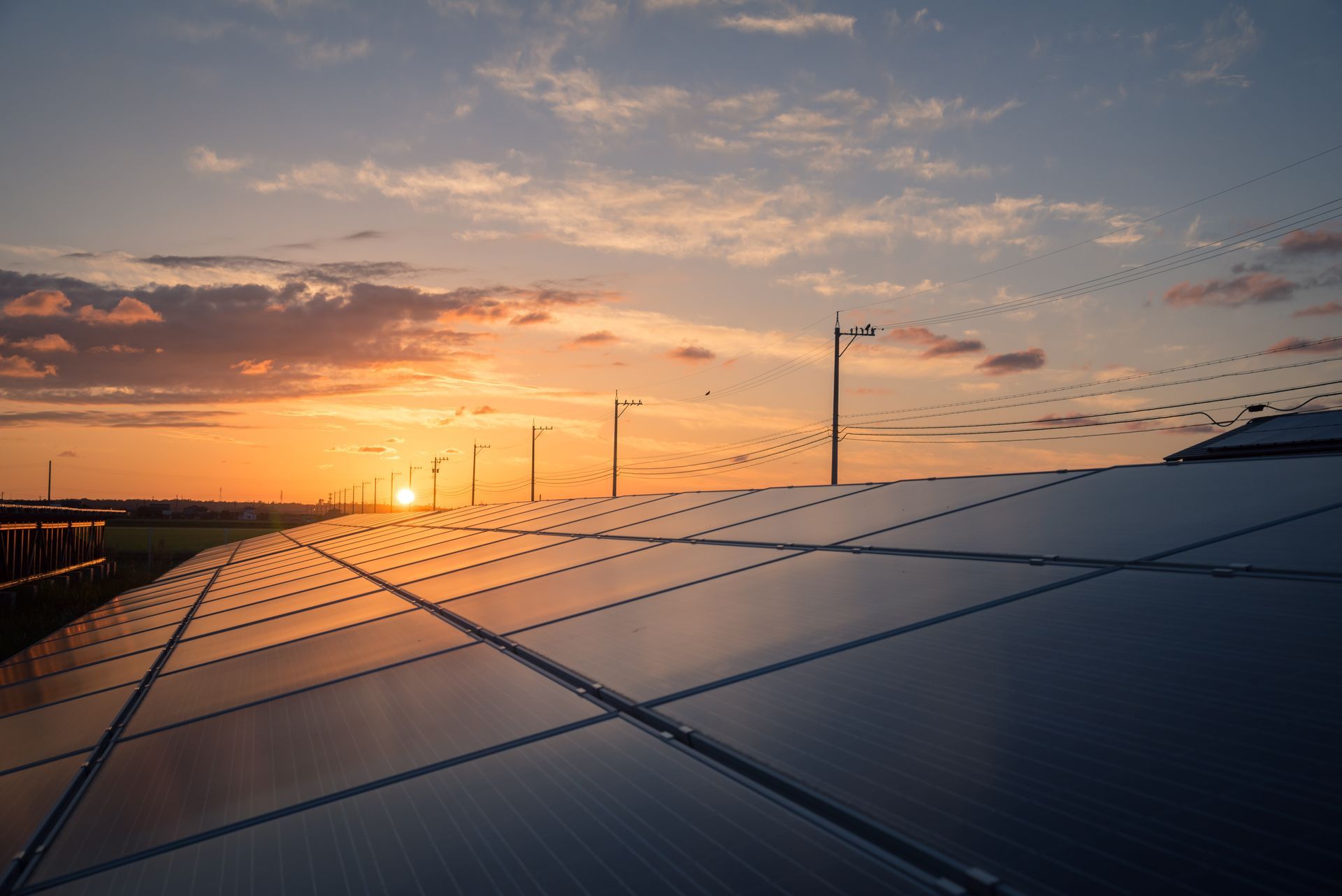 Solar panels at sunset reflecting the orange sky. Power poles visible in the distance.