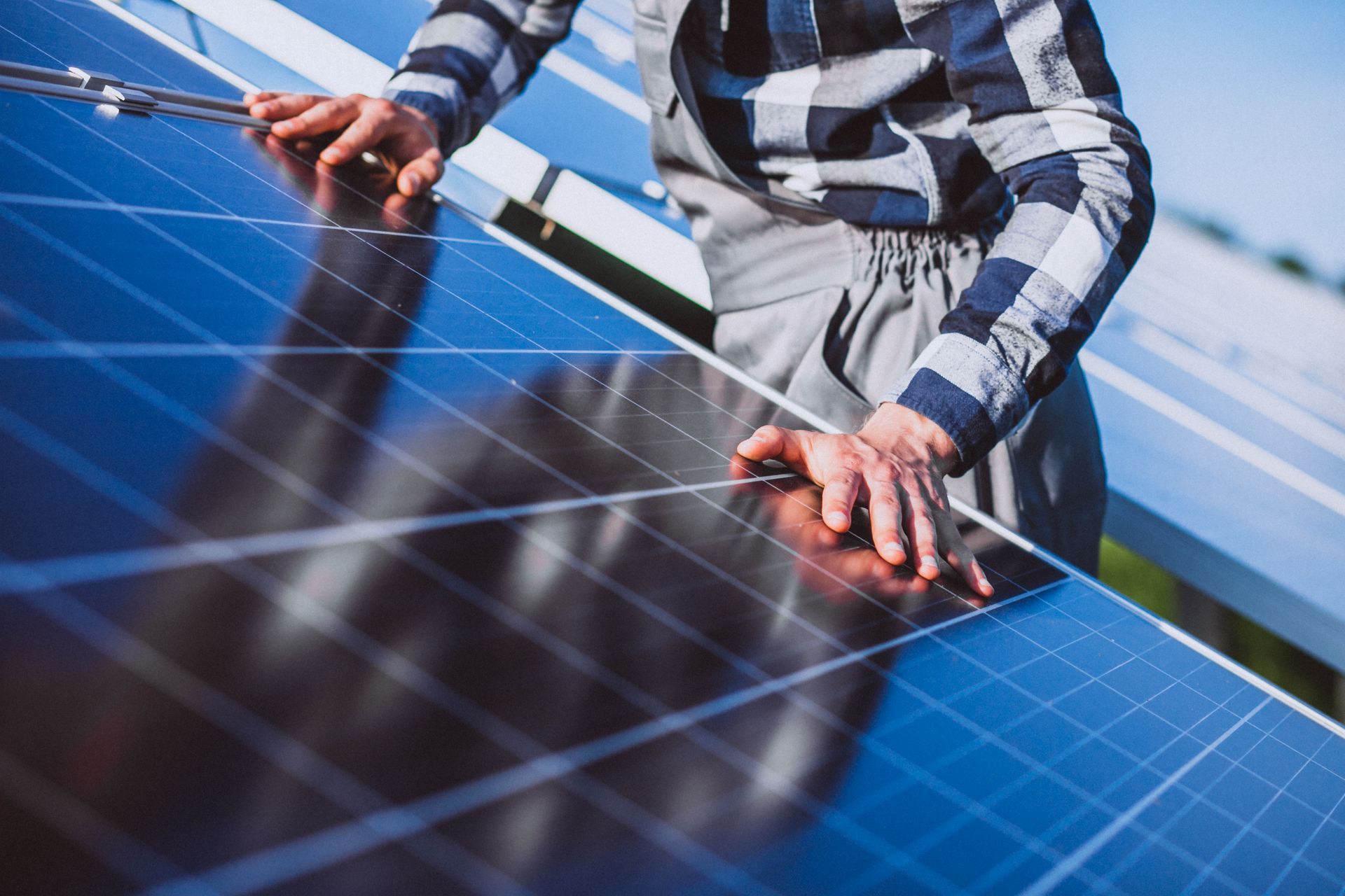 Person in plaid shirt working on a solar panel installation outdoors.