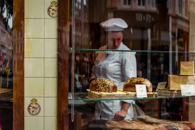 Une artisane boulangère-patissière, aperçue à travers la vitrine d'une boulangerie.