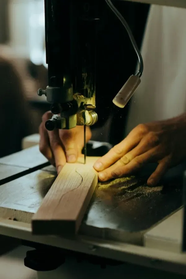 Un artisan ébeniste utilise une scie à ruban pour découper une forme courbe dans une planche de bois sur une table d'atelier.