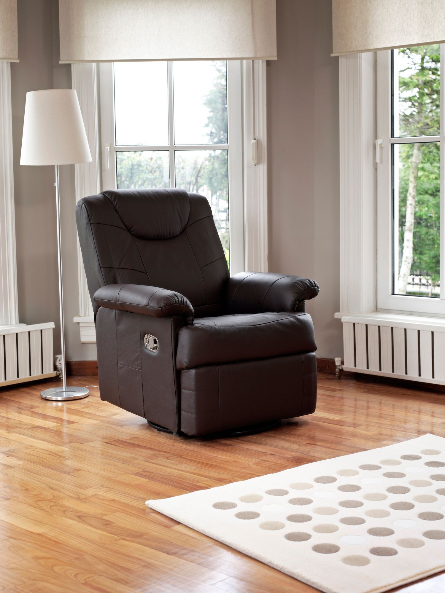 Brown recliner in a room with a window, rug, and floor lamp. Brown recliner in a room with a window, rug, and floor lamp.