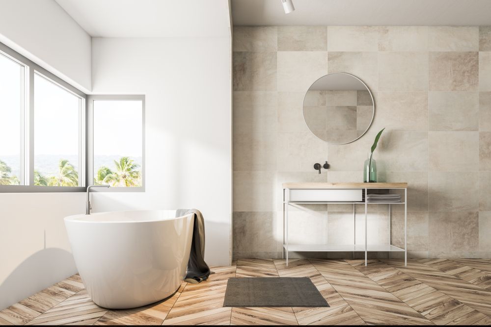 Bright modern bathroom with a freestanding tub, round mirror, and beige tiled wall — Hinch Plumbing In Breakwater, VIC