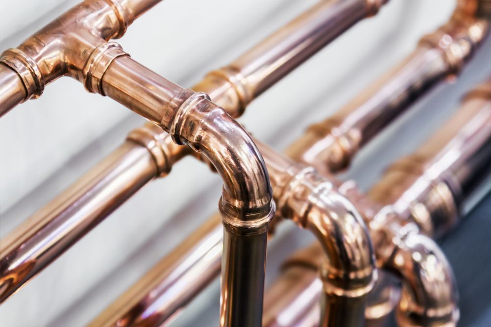 Close-up of shiny copper pipes with elbow joints and parallel tubing against a white background — Hinch Plumbing In Breakwater, VIC