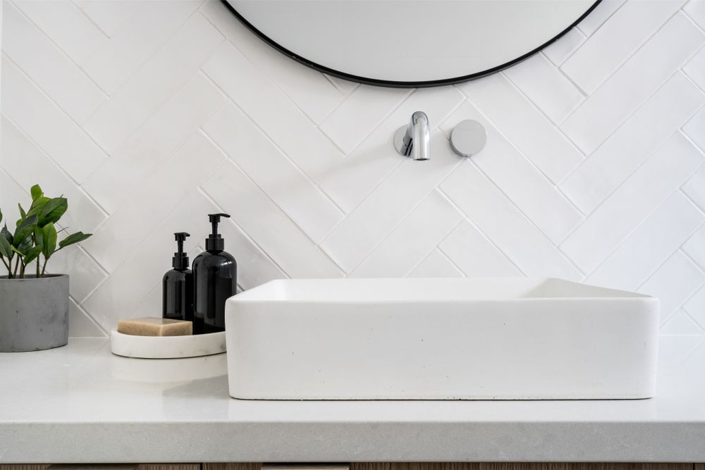 Modern white bathroom sink with mirror, soap dispensers, and a small potted plant — Hinch Plumbing In Breakwater, VIC