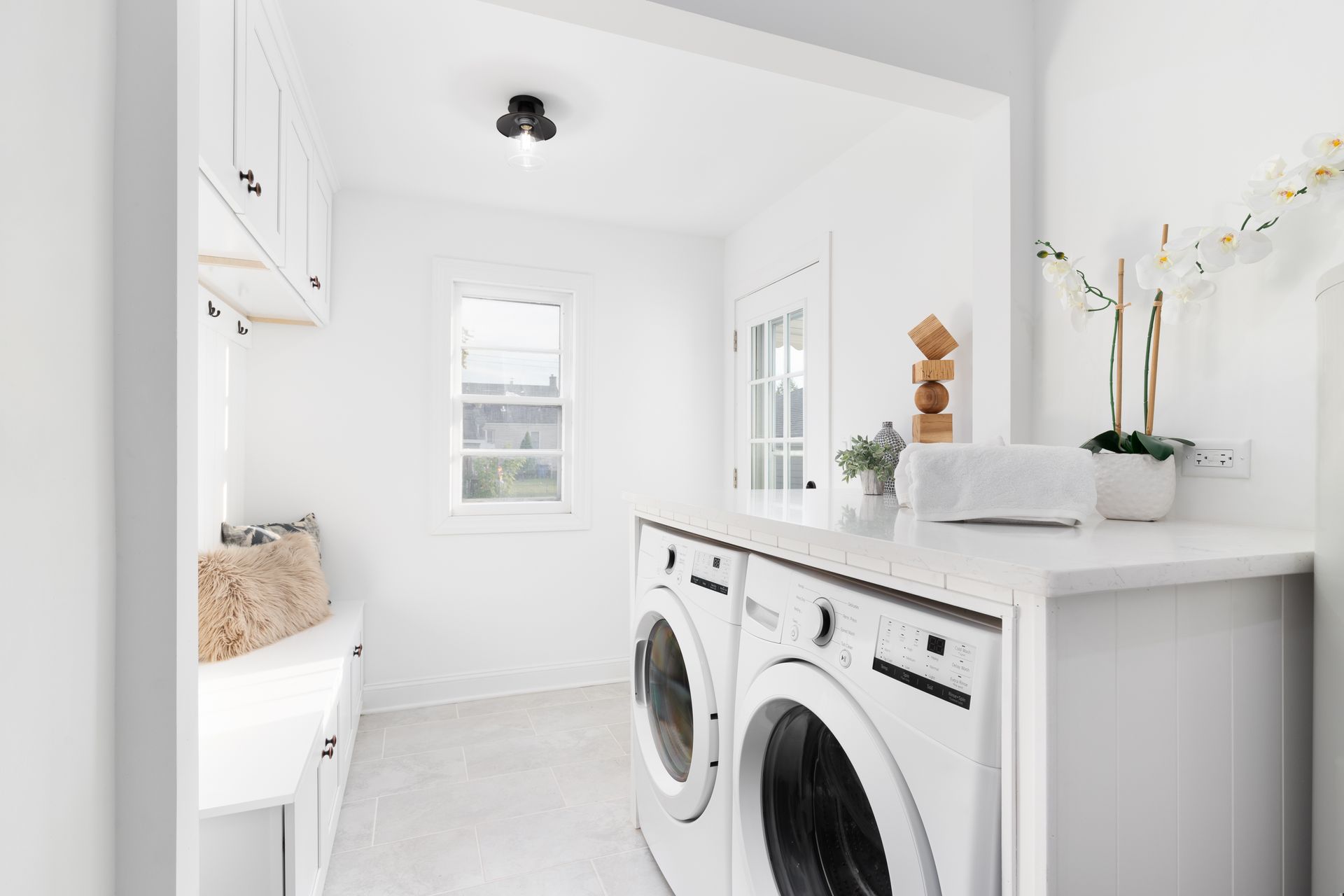 Bright white laundry room with stacked washer and dryer, sink, cabinets, and window — Hinch Plumbing In Breakwater, VIC