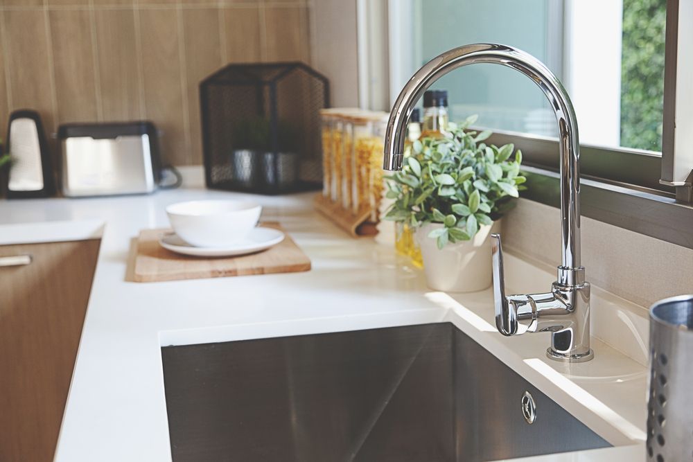 Modern kitchen sink with chrome faucet, white countertop, and potted plant by a window — Hinch Plumbing In Breakwater, VIC