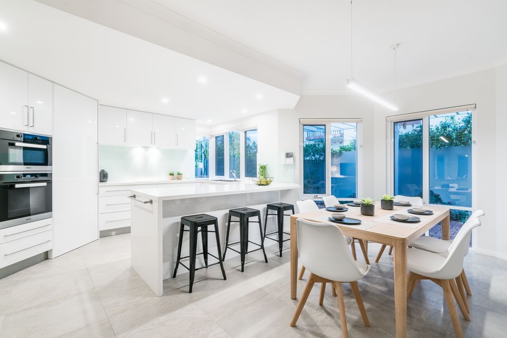 Bright modern white kitchen and dining area with island, bar stools, and large windows — Hinch Plumbing In Breakwater, VIC
