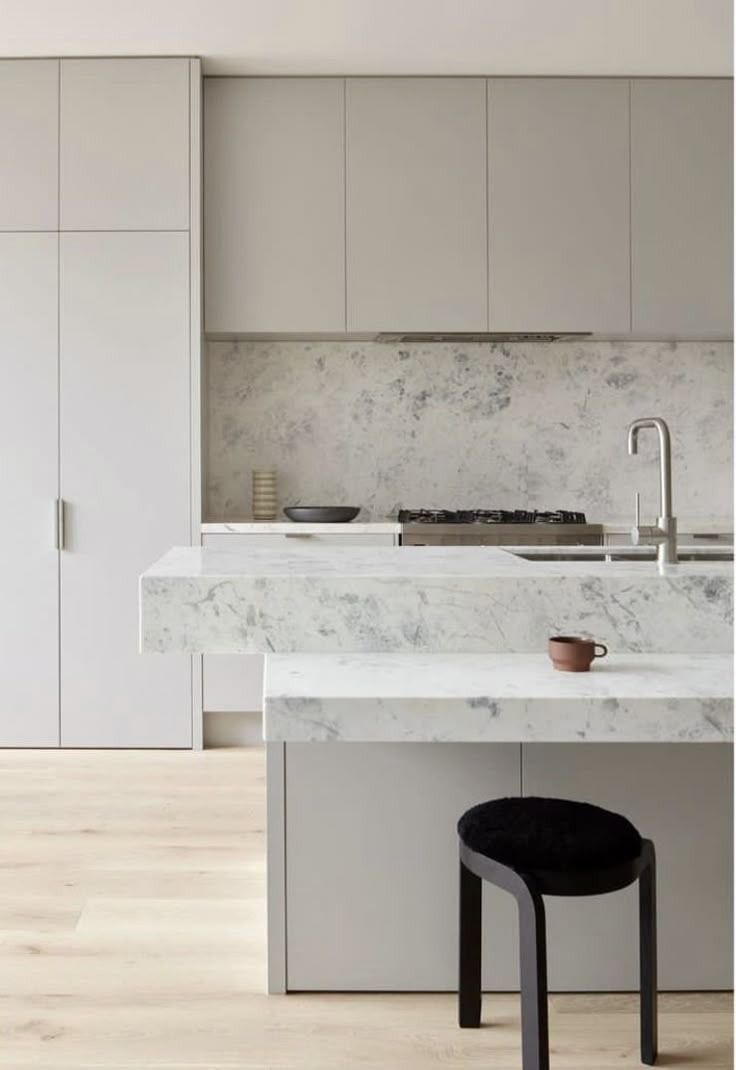 Minimal white modern kitchen with marble island, black stool, and light wood floors — Hinch Plumbing In Breakwater, VIC