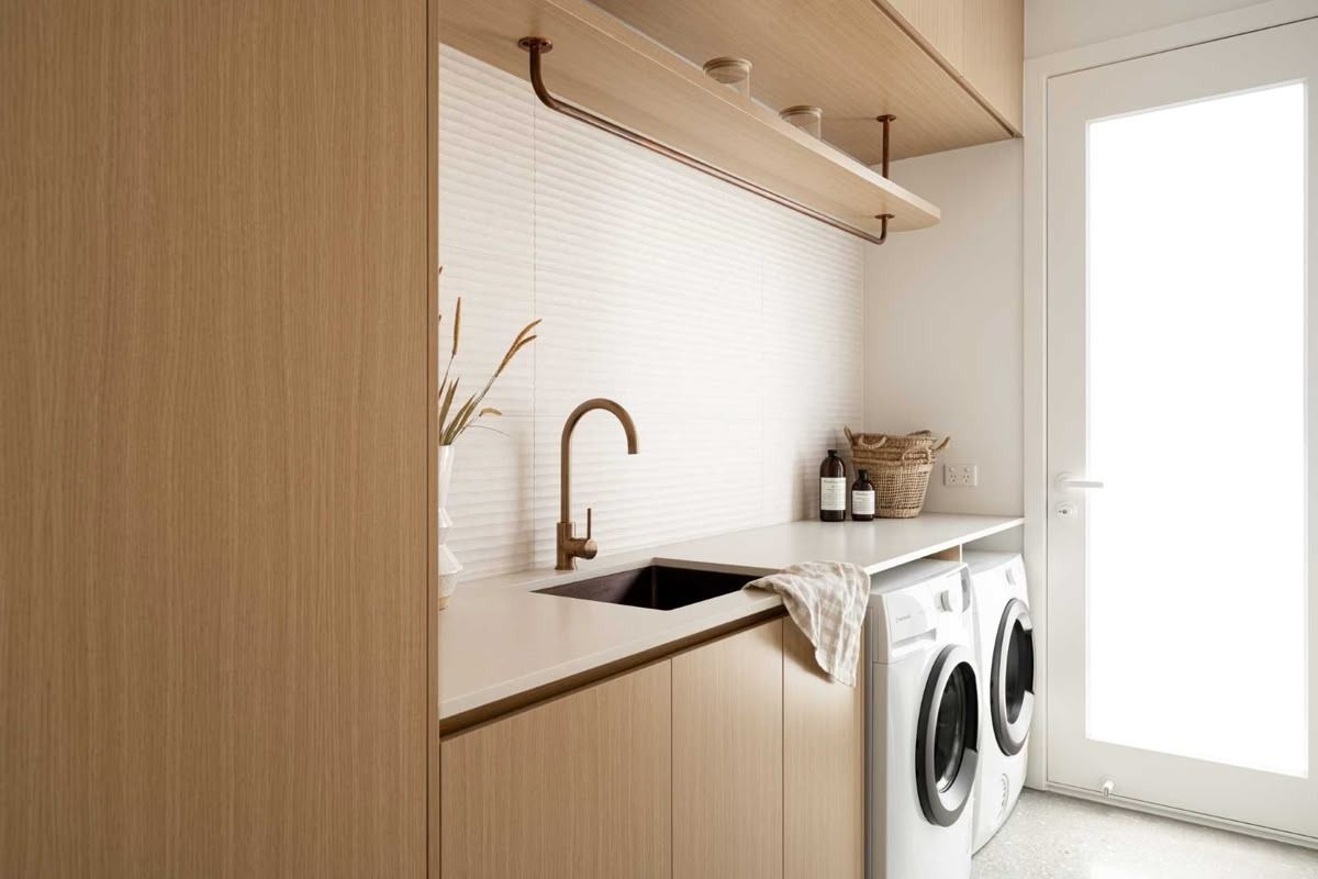 Bright laundry room with wood cabinets, sink, countertop, and front-loading washer and dryer. — Hinch Plumbing In Breakwater, VIC