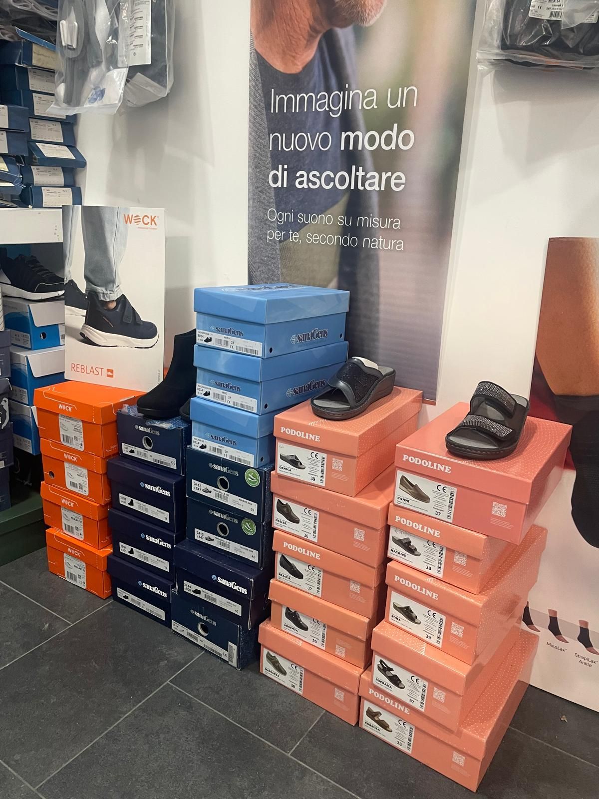 Scarpe in scatole di vario tipo, accatastate sul pavimento di un negozio. Colori: blu, arancione, rosa.