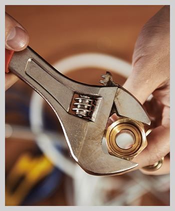 Hands using an adjustable wrench to tighten a brass fitting.