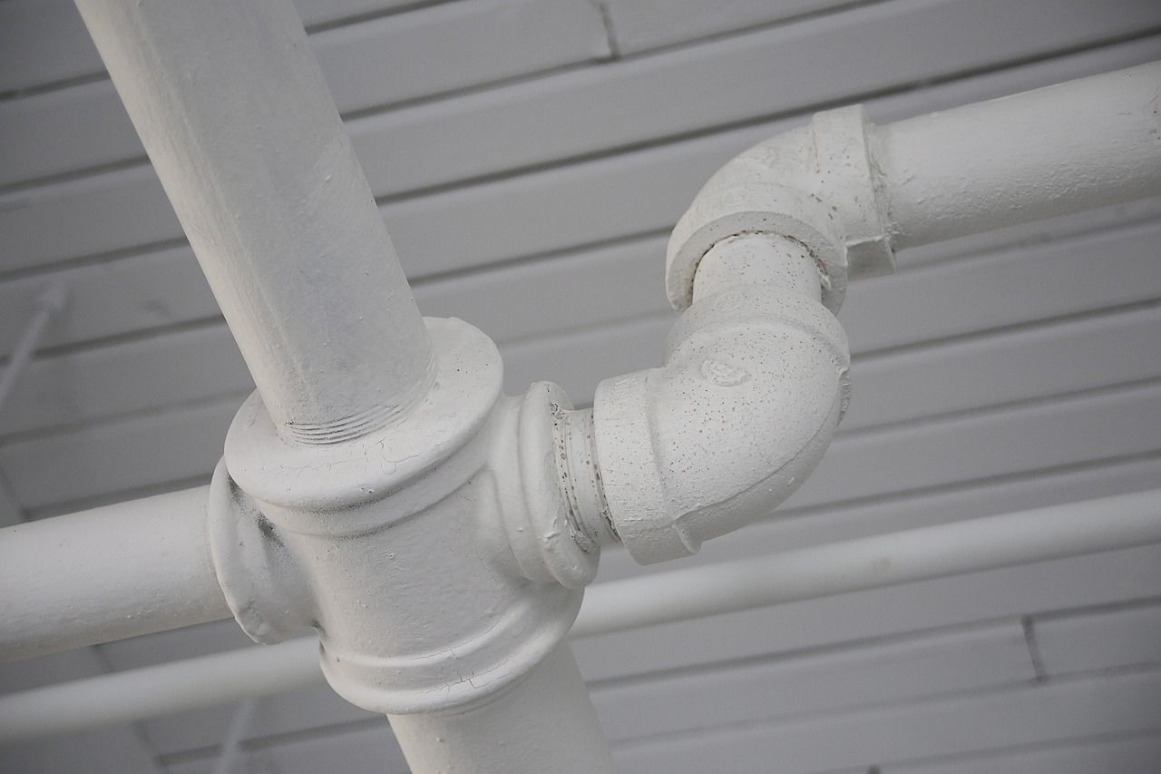 White painted pipes and fittings against a white slatted ceiling.