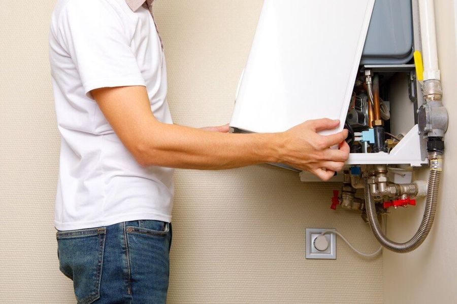 A man is fixing a water heater on the wall.