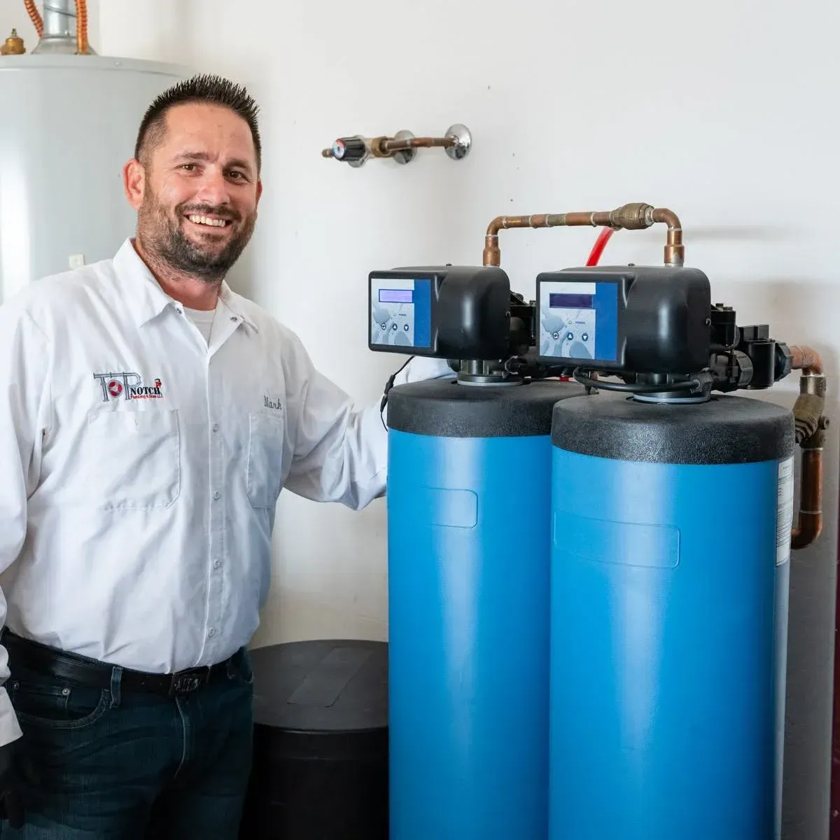 Technician standing beside two blue water treatment tanks with control units in a utility room