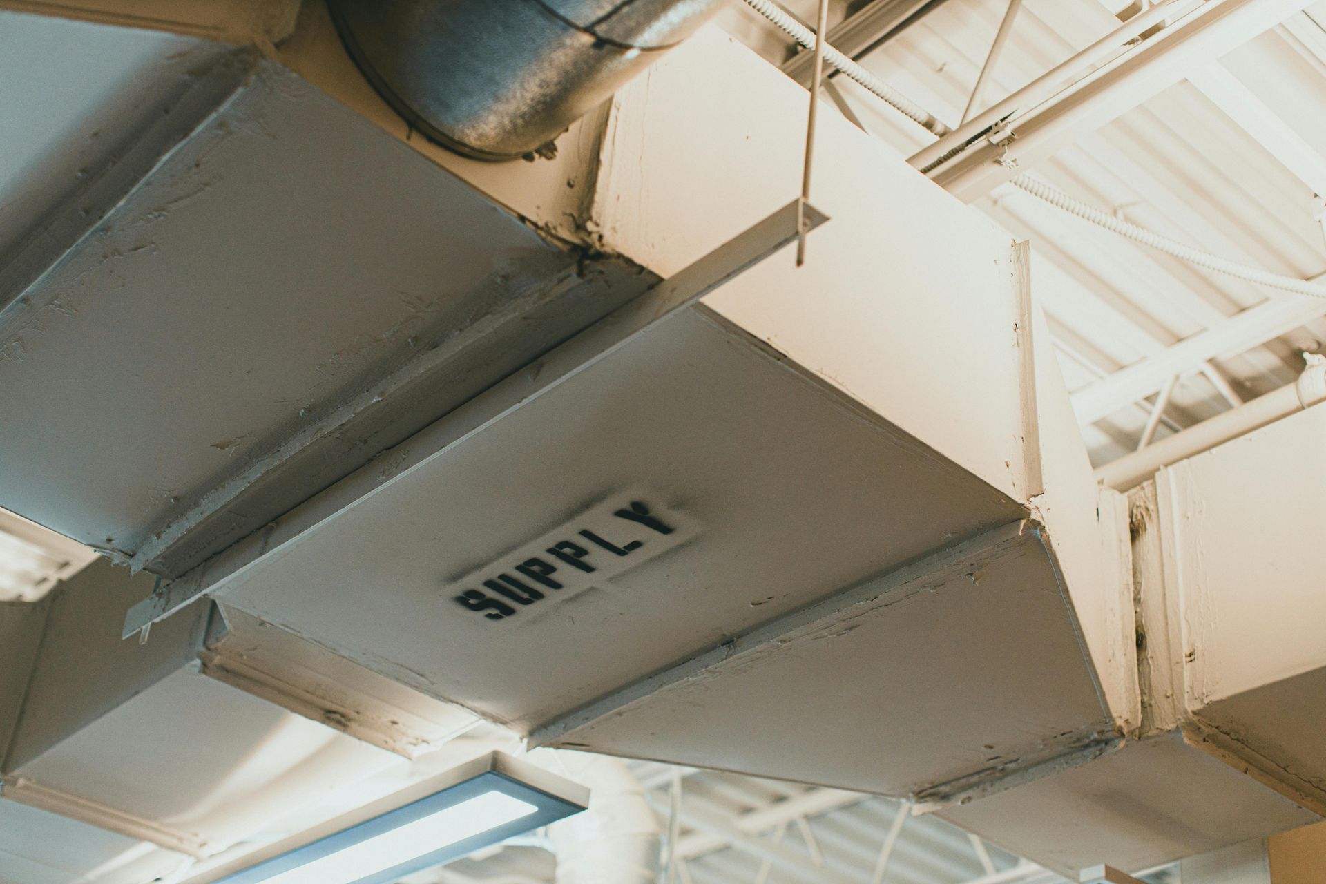 A section of industrial HVAC ductwork suspended from a ceiling, with the word